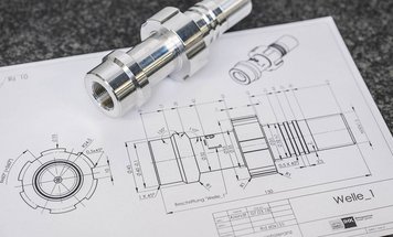 A polished metallic component is positioned on a technical drawing featuring detailed measurements and specifications. The drawing outlines various angles and dimensions related to the part labeled "Welle_1," indicating its design and engineering details.