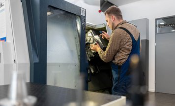 A technician in blue overalls is working on a large machine, inspecting its internal components with a tool. The setting appears to be a modern workshop, showcasing the focus on mechanical maintenance and precision.